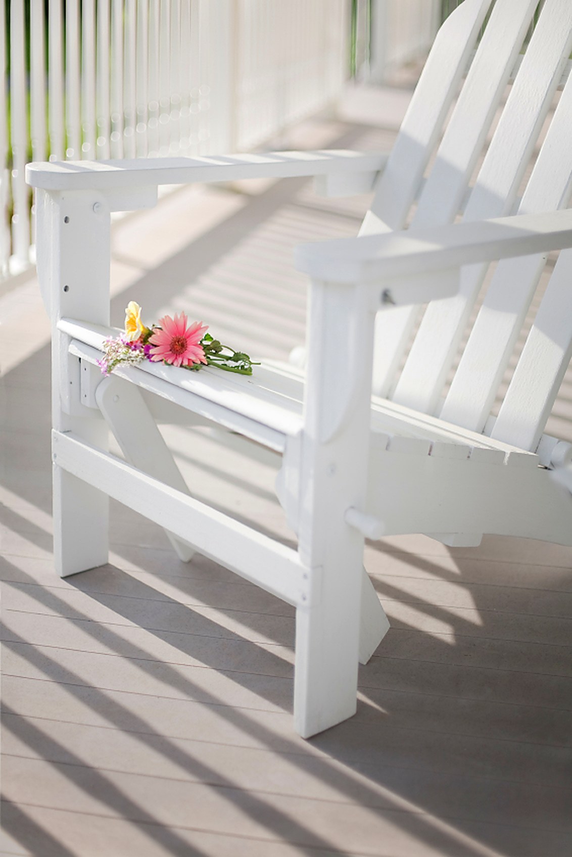 White Adirondack chair on a cellular PVC porch deck in sunlight.